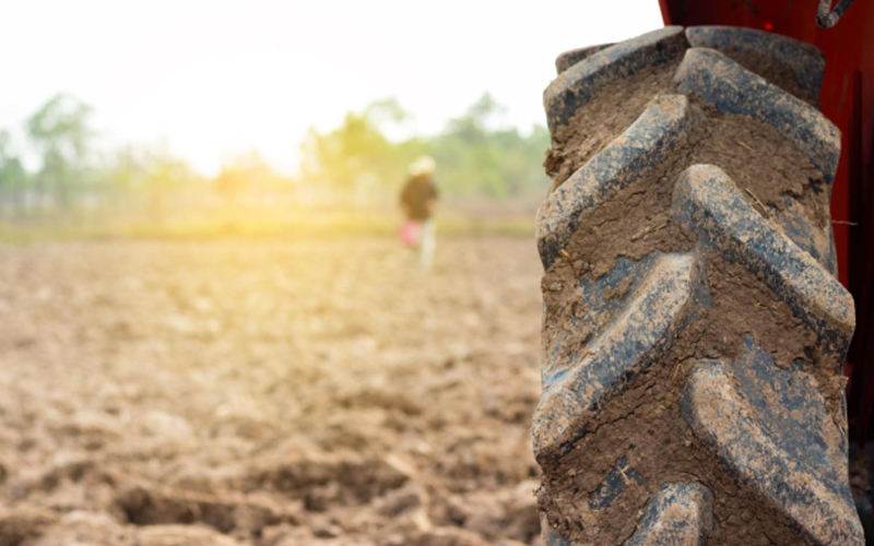 Un tractor embarrado con neumáticos grandes arando un campo fértil, preparando el suelo para plantar.